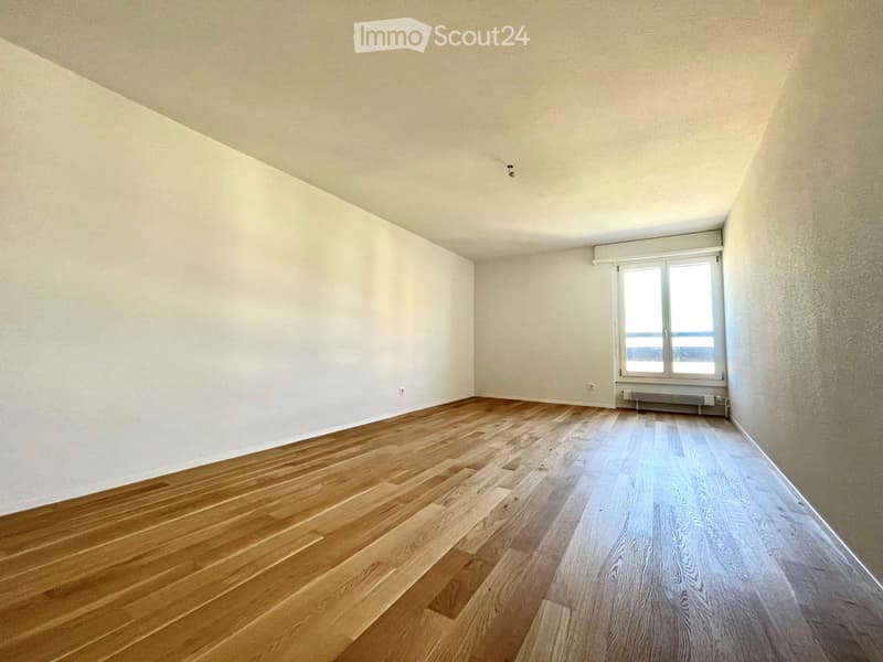 Empty room with wooden flooring, white walls, and a large window with a view.