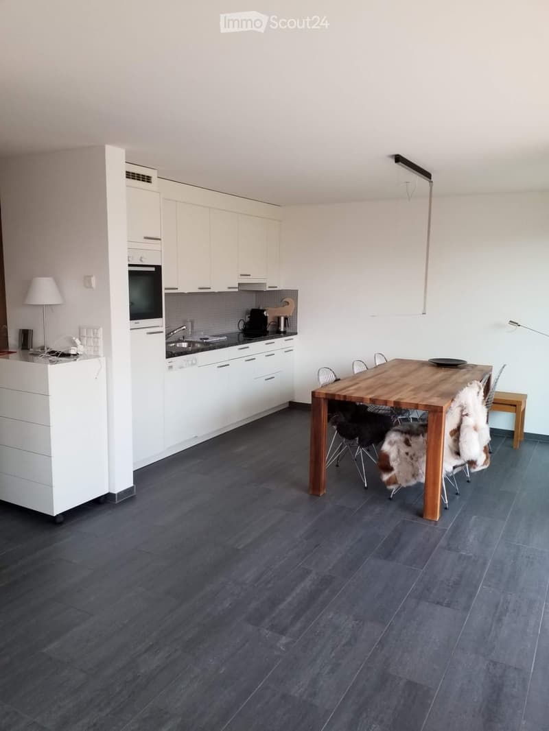 Modern kitchen with white cabinets, dark wooden floor, and a dining area with a wooden table and chairs.