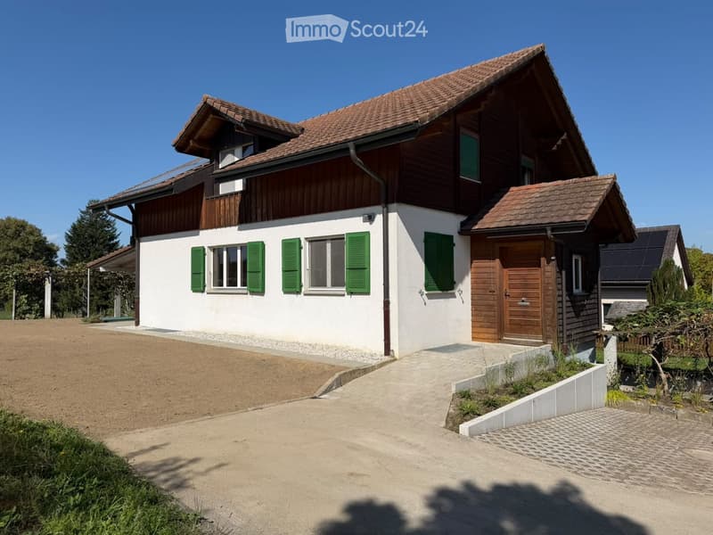 Two-story house with white walls, green shutters, wooden door, and solar panels on the roof.