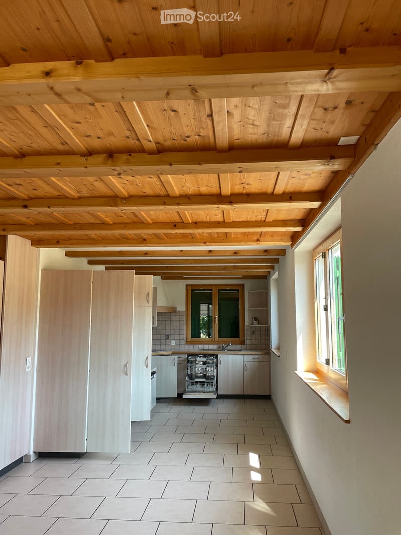 Bright kitchen with wooden ceiling beams, tiled floor, white cabinets, and a built-in dishwasher.