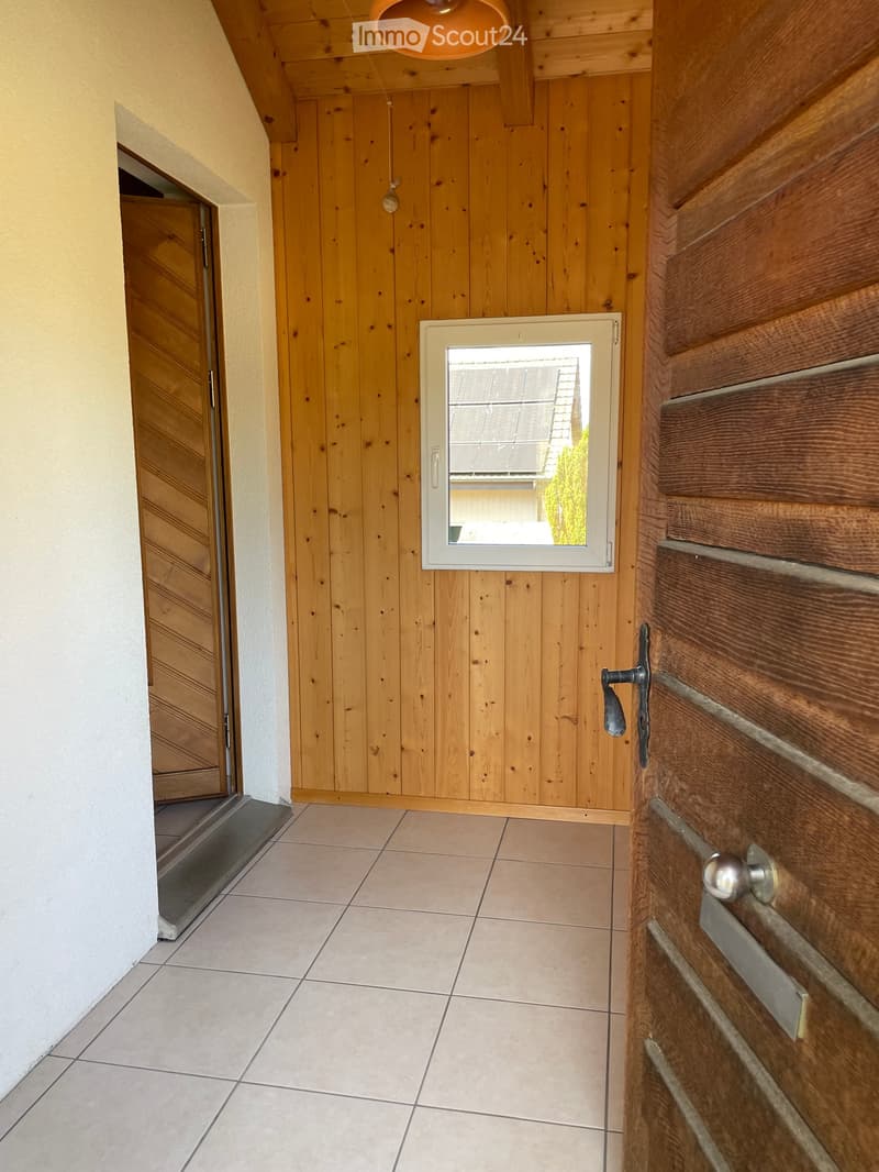 A narrow hallway with wooden panel walls, tiled floor, and a small window showing a view of the roof and surrounding area.