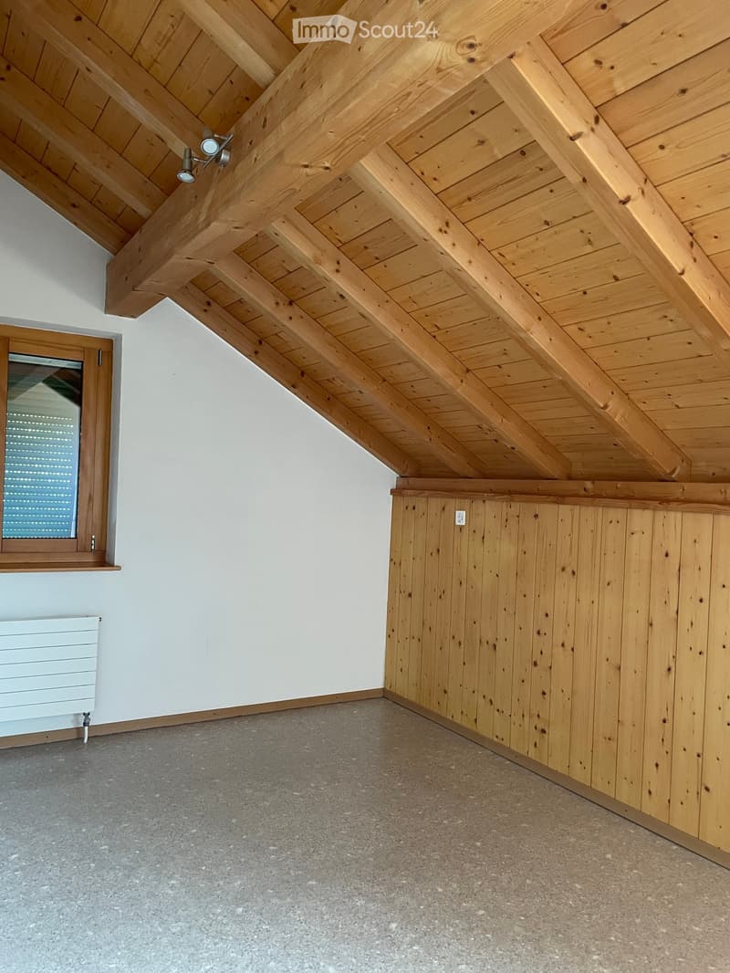 Empty room with exposed wooden beams on the ceiling, grey concrete floor, white walls, and a small window with blinds.