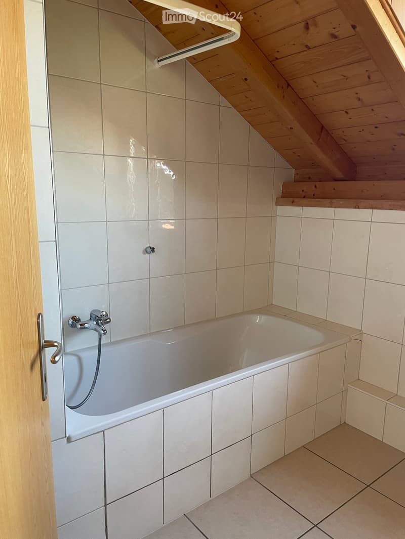 Bathroom with a white bathtub, tiled walls, and a wooden staircase leading upwards.