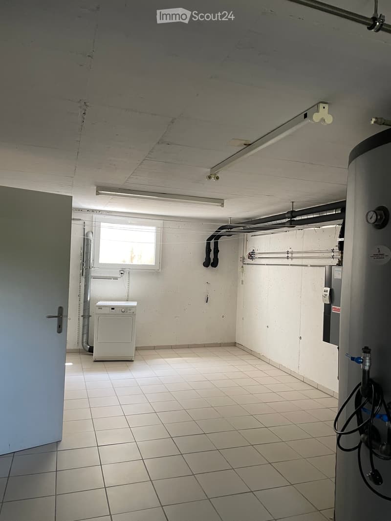 Utility room with tiled floor, white walls, a washing machine, and various pipes and fixtures.