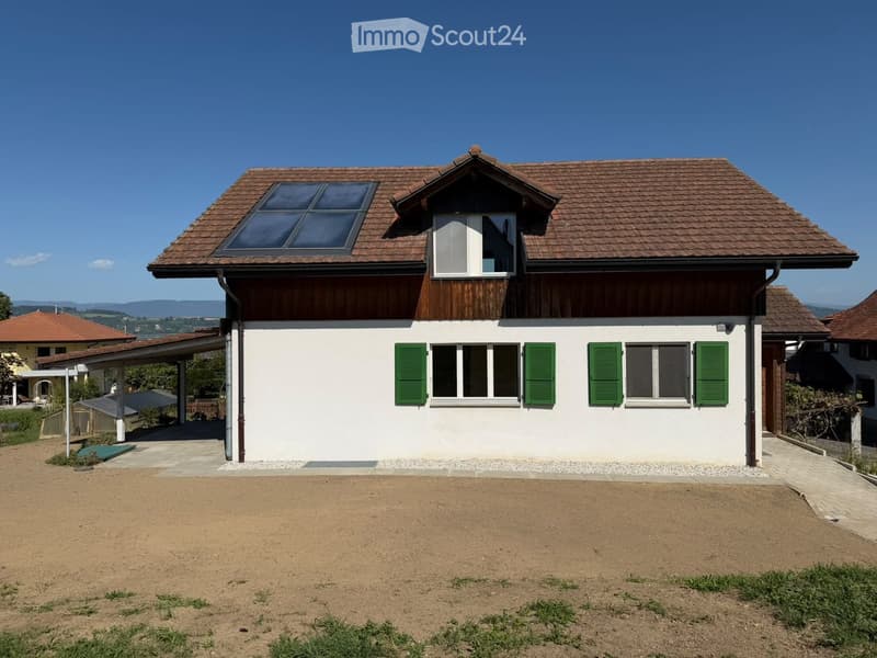 Two-story house with white walls, green shutters, and a brown tiled roof. Features a covered entrance and a driveway.