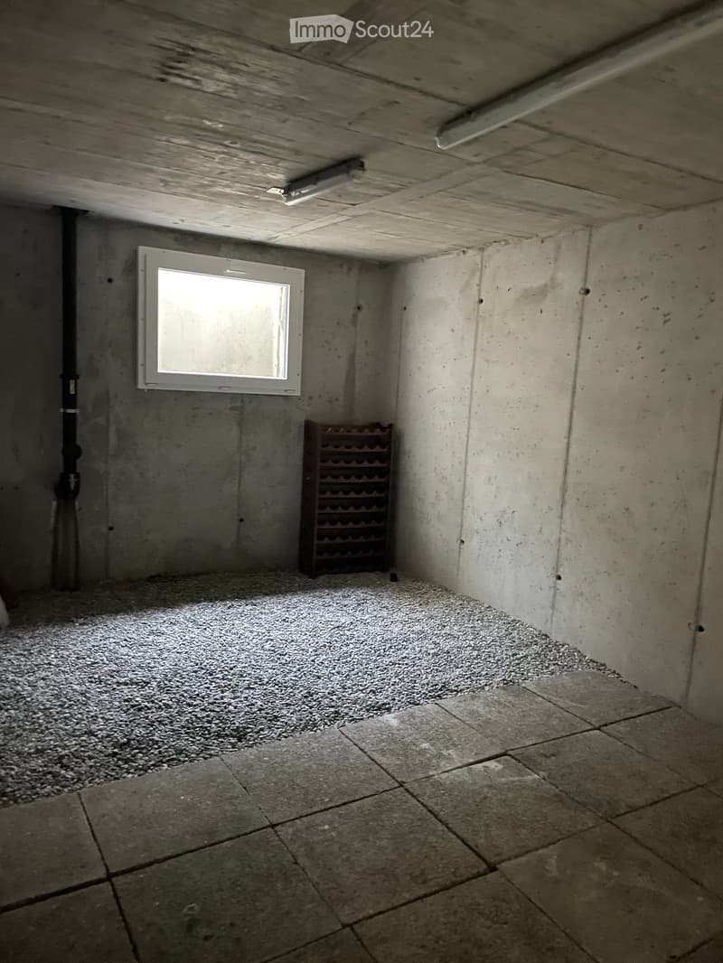 Small, unfinished basement or cellar with concrete walls, a single window, a wine rack, and a mix of gravel and tiled flooring.