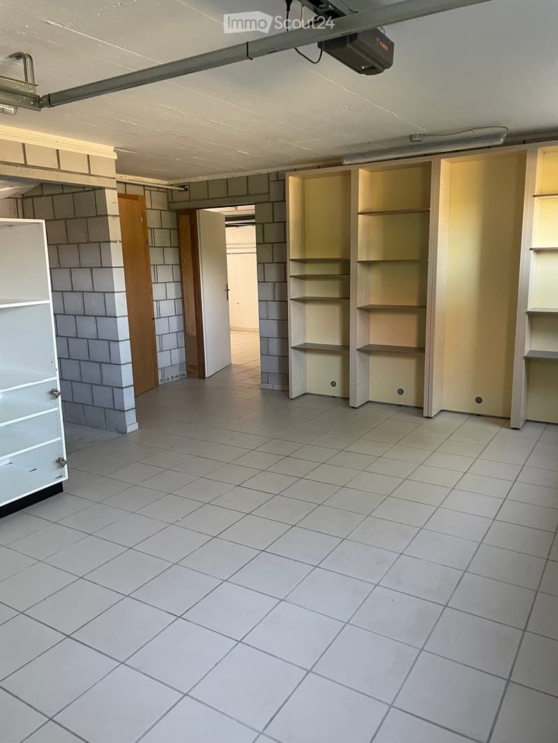 Empty room with tiled floor, exposed brick walls, built-in shelves, and a wooden door leading to another space.