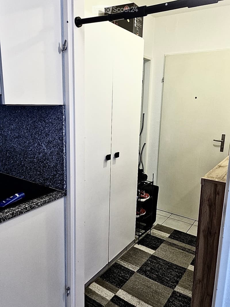 Hallway with white walls, tiled flooring, and a storage cabinet or closet. A garage or storage area is visible through the open doorway.