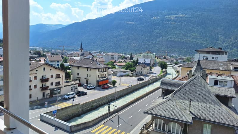 Balcony overlooking a town with buildings, roads, and a mountainous backdrop.