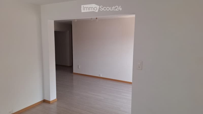 Empty room with white walls, wooden flooring, and a doorway leading to another room.