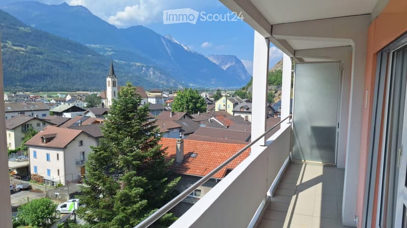Balcony overlooking a town with red-tiled roofs, a church spire, and distant mountains.