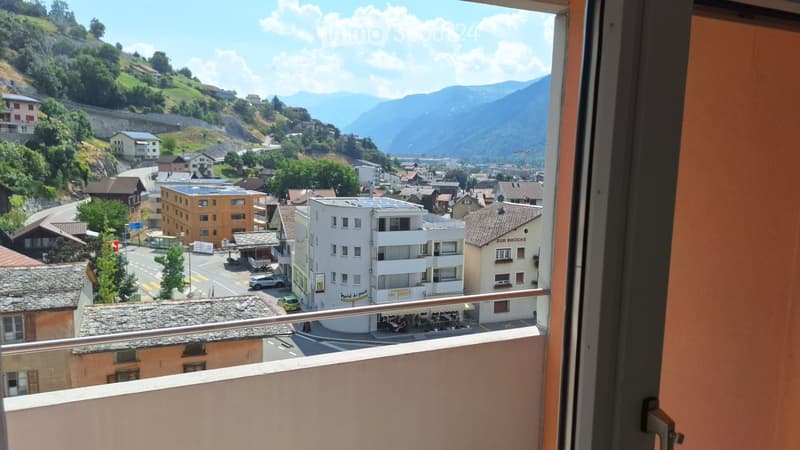 Balcony overlooking a town with buildings, cars, and distant mountains.
