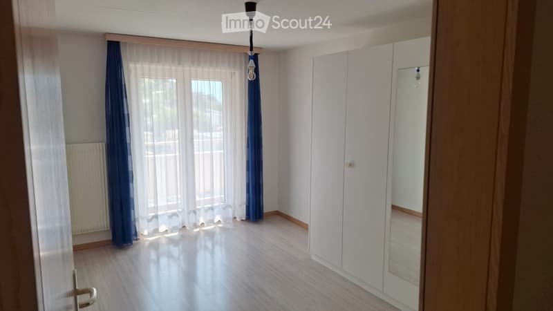 Empty room with wooden flooring, white walls, large windows with sheer curtains, and built-in white closet with mirrored door.