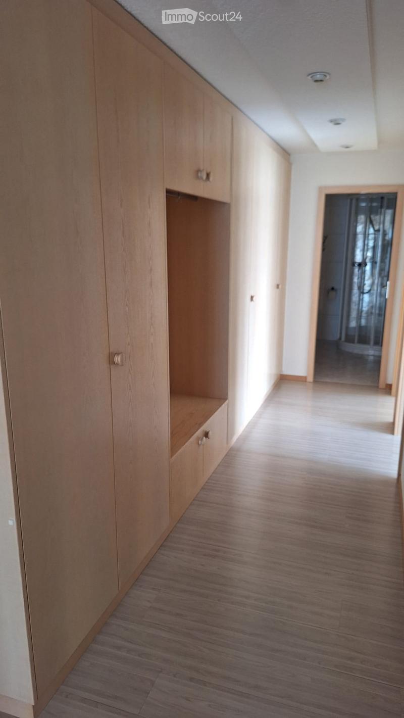 Empty hallway with wooden flooring, built-in wooden storage units, and a door leading to another room.