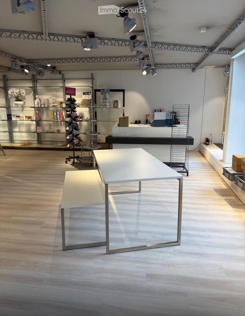 Modern, minimalist room with wooden flooring, white tables, glass shelves, and decorative items.