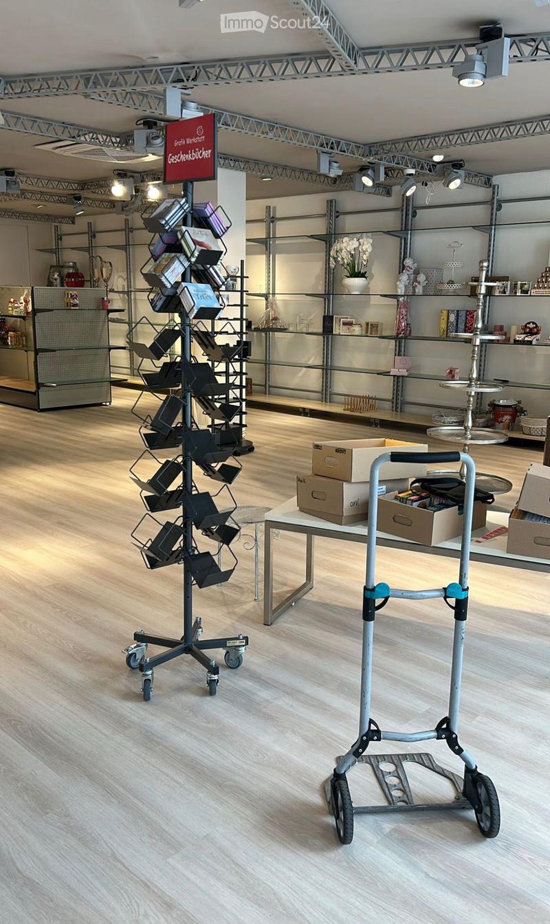 Modern interior with wooden flooring, glass display shelves, a cart, a table with boxes, and a vase with flowers.