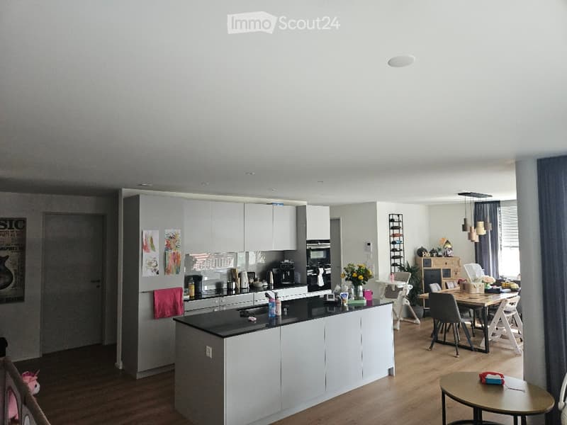 Modern kitchen with white cabinets, black countertop, and a central island. There is a dining area with a table and chairs, a coffee maker, and decorative items on the counter.