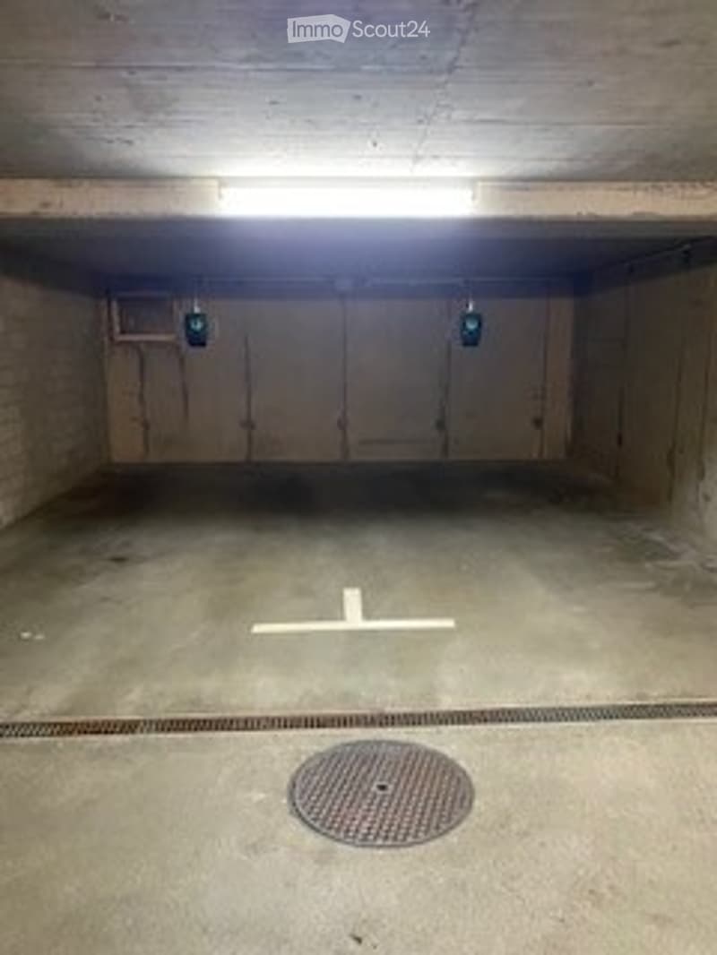 Underground parking space with concrete walls, a single marked parking spot, and a central drainage grate.