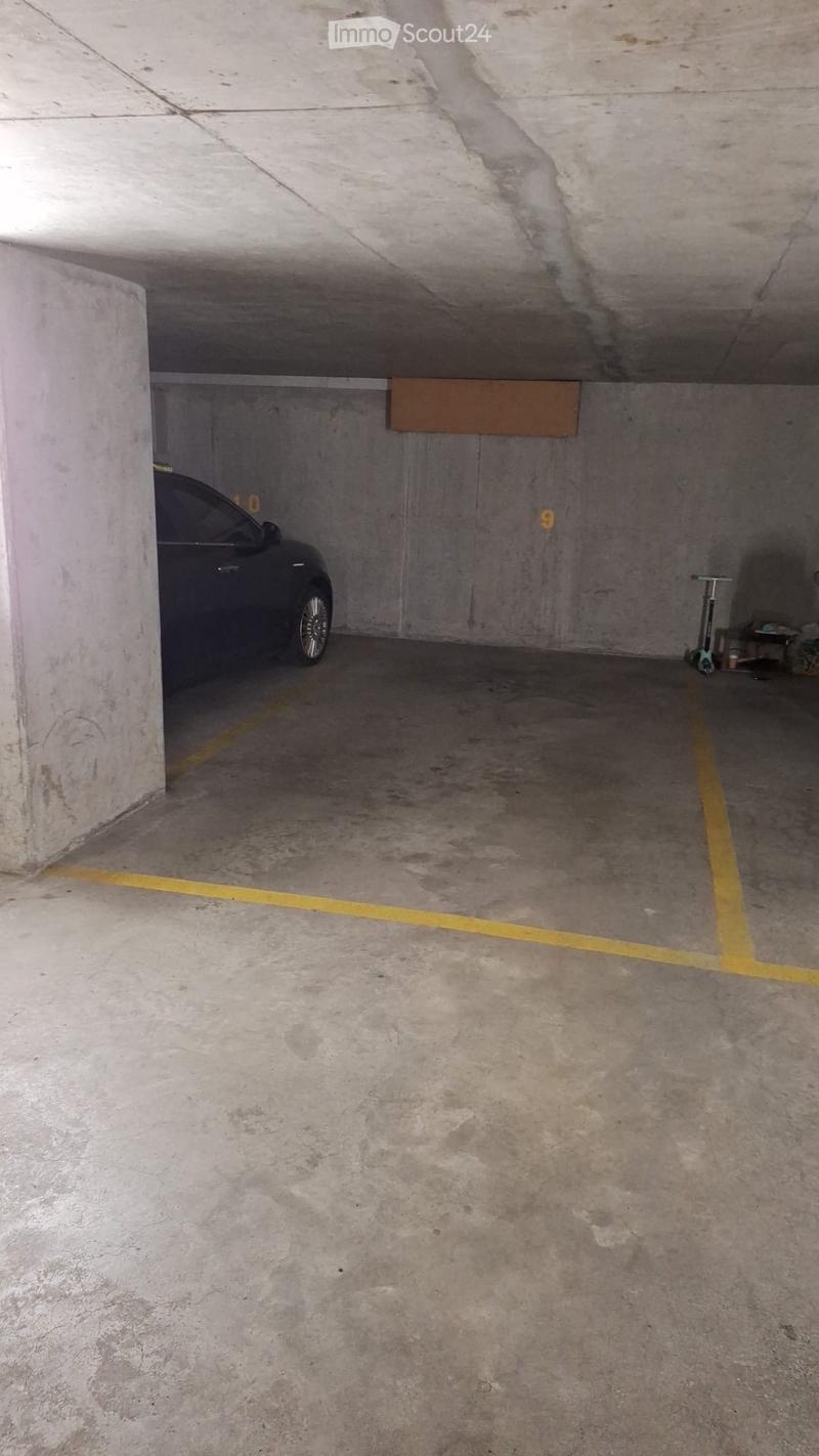 Underground parking space with concrete walls and floor, marked parking spots, and a parked car and scooter.