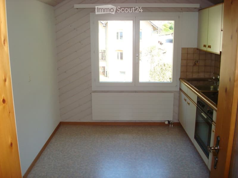Empty kitchen with white tiles, white cabinet, and brown wall. Big window with outdoor view.