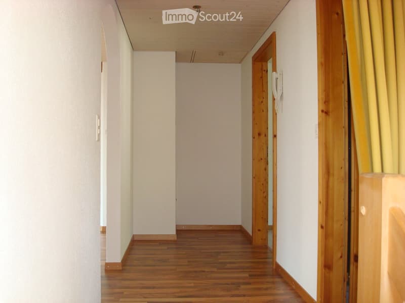 Empty hallway with wooden flooring, white walls, and wooden doors. A white telephone is mounted on the right wall.