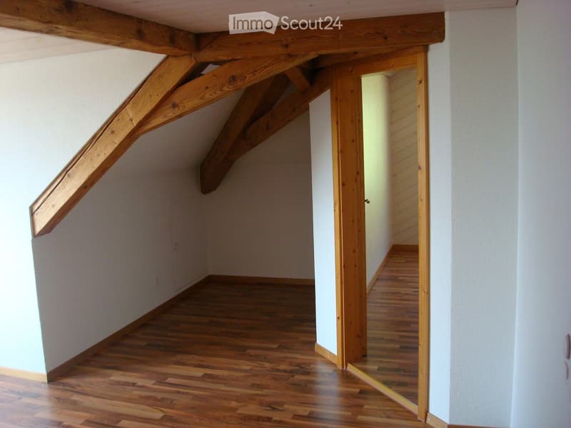 a room with wooden floor, wooden ceiling beams, white walls, and a mirror