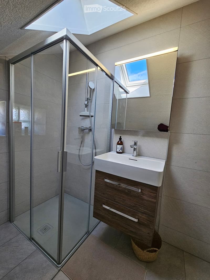 Bathroom. Modern bathroom with a white sink, wooden cabinet, glass shower enclosure, and skylight window above the mirror.