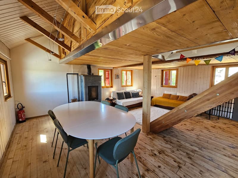 Furnished Room. Open-plan living and dining area with wooden beams, a round dining table with chairs, a sofa, a bed, and a fireplace.