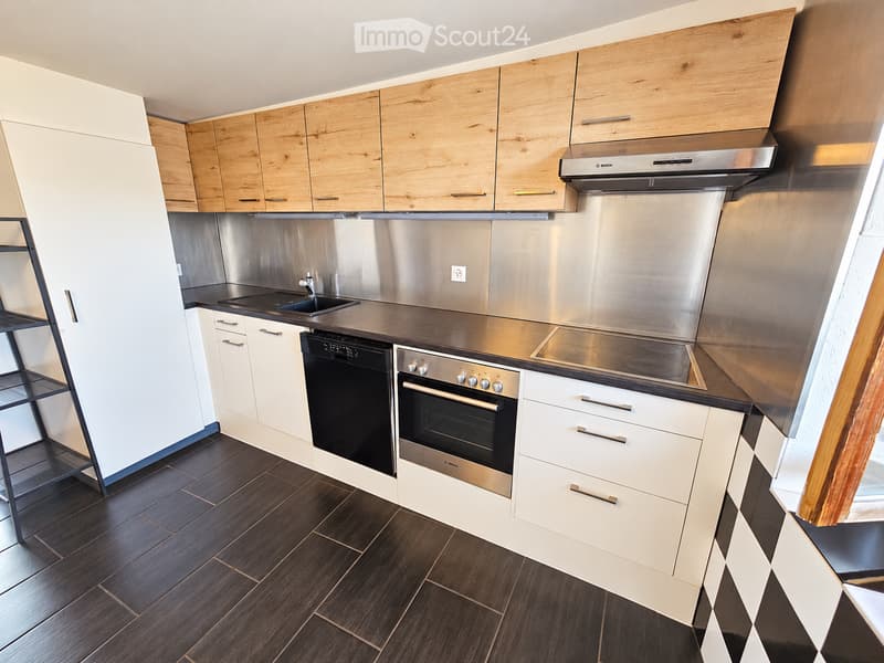 Modern kitchen with light wooden cabinets, stainless steel appliances, and dark wooden flooring.
