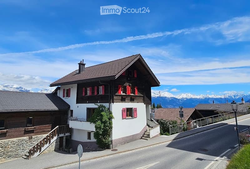 House. Traditional Swiss house with red shutters, white walls, and a tiled roof, situated in a scenic mountain landscape.