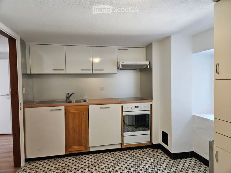 Kitchen. Compact kitchen with white cabinets, wooden accents, a sink, oven, and range hood. The floor features a black and white checkered tile pattern.
