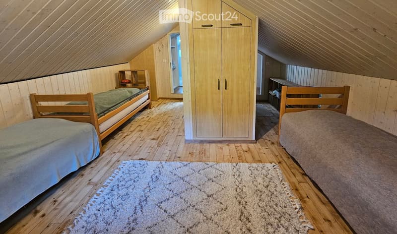 Bedroom. Cozy attic bedroom with wooden walls and slanted ceilings, featuring two single beds, a wardrobe, and a small shelf.