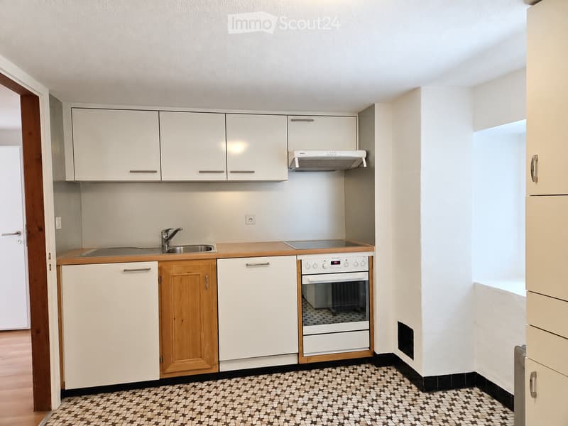 Modern kitchen with white cabinets, wooden accents, stainless steel sink, oven, and range hood. The floor features a patterned tile design.