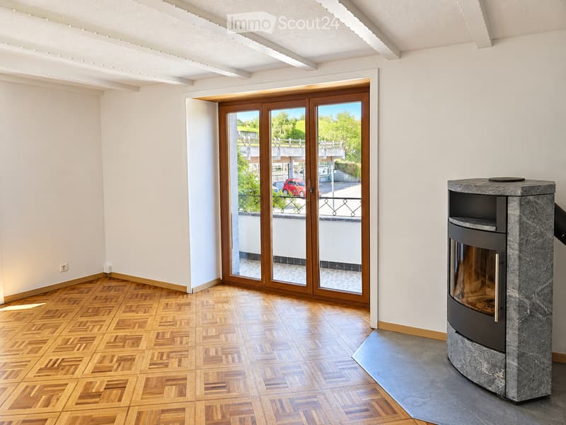Bright room with wooden herringbone flooring, large glass sliding doors leading to a balcony with a scenic view, and a modern stone fireplace.