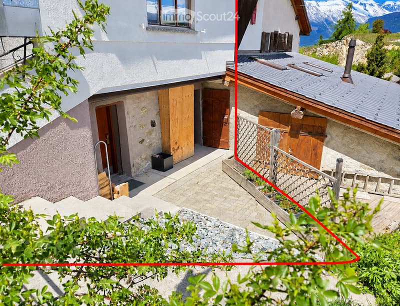 A two-story house with a stone facade, wooden doors, and a metal roof, situated in a mountainous area with a view of snow-capped peaks.