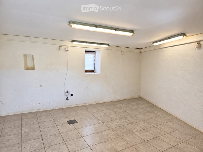 Empty room with tiled floor, white walls, and fluorescent lighting. Features a small window with blinds and electrical outlets.