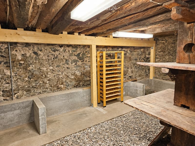 The room features exposed wooden beams, stone walls, a wooden shelf, and a wooden table with a stone top.