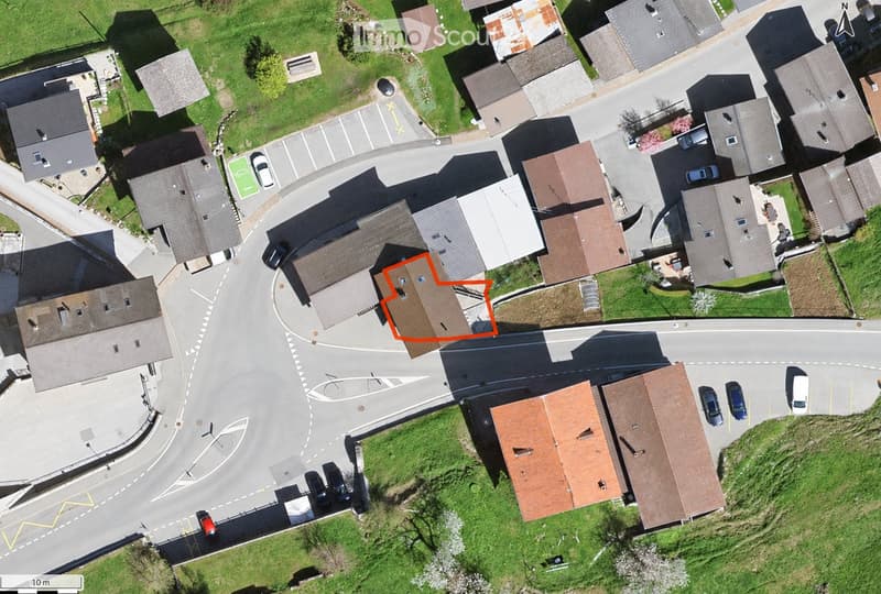 Aerial view of a residential area with multiple houses, roads, and parked cars. The highlighted house is a two-story structure with a brown roof and multiple windows.