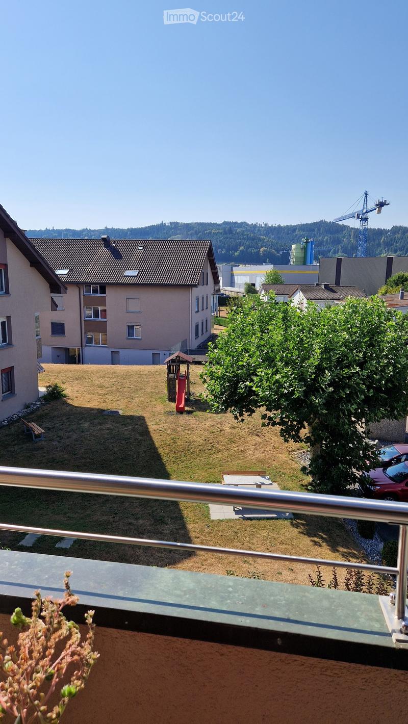 View from a balcony overlooking a grassy yard with a small play structure, benches, and surrounding residential buildings.