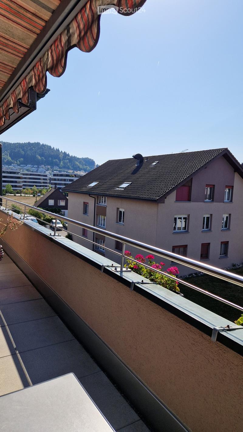 Balcony with metal railing, potted plants, and a view of neighboring houses and greenery.