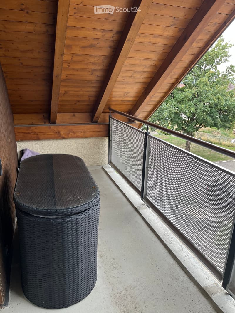 Balcony with wooden ceiling, metal railing, and a single wicker chair.