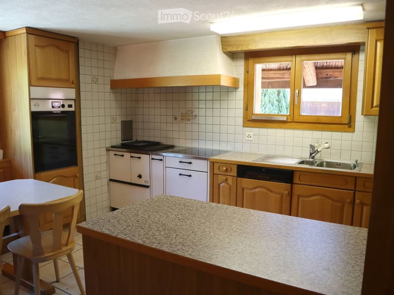 Kitchen with wooden cabinets, granite countertop, oven, dishwasher, sink, and a small dining area with a table and chairs.