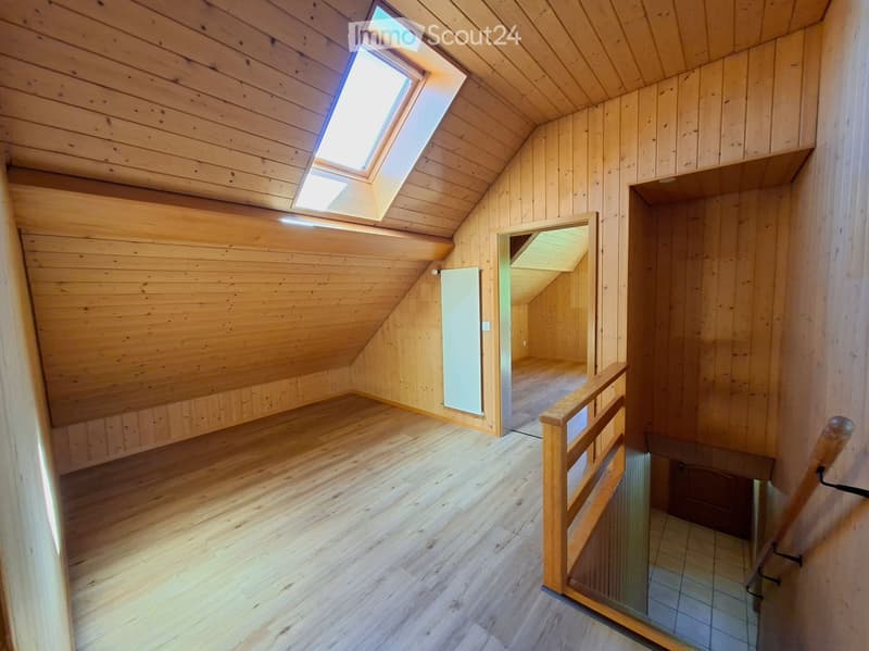 Empty attic space with wooden walls and ceiling, skylight window, wooden floor, and a staircase leading down.