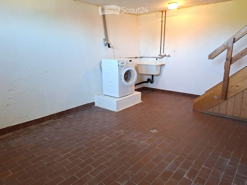 Small bathroom with a washing machine and a sink, featuring red tiled flooring and white walls.