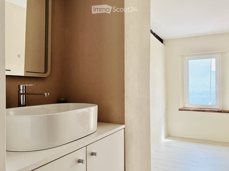 Modern bathroom with a white sink, sleek faucet, and built-in cabinets. A window offers a scenic view.