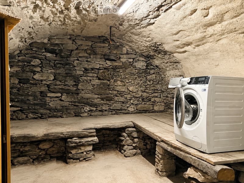 A rustic bathroom with stone walls and a wooden platform holding a modern washing machine.
