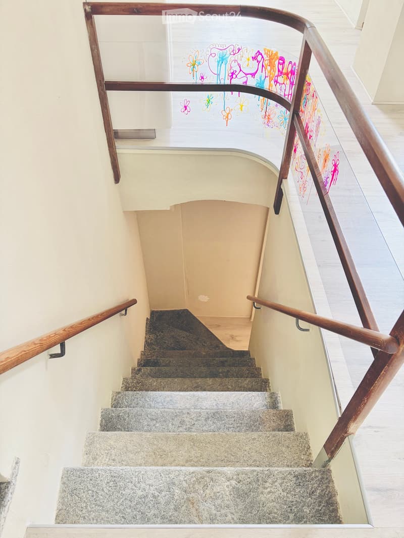 Spiral staircase with wooden handrails and granite steps, featuring colorful abstract artwork on the glass railing.