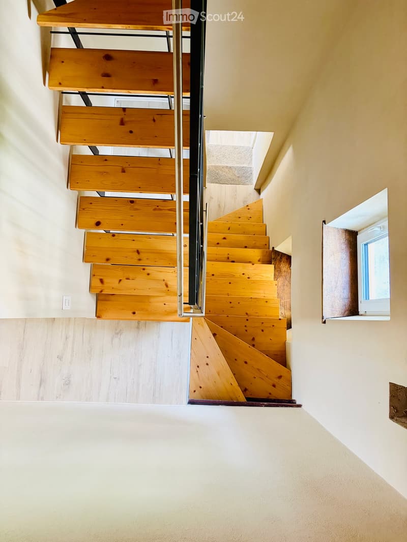 Wooden staircase with metal railing, light-colored walls, and a small window on the right side.