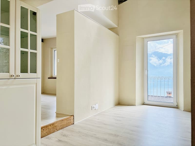 Empty room with light-colored walls, wooden flooring, and a sliding glass door leading to a balcony with a scenic view.
