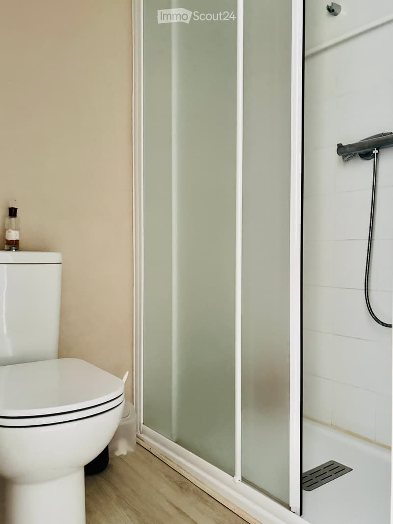 Modern bathroom with a white toilet, glass shower enclosure, and a small bottle on the toilet tank.
